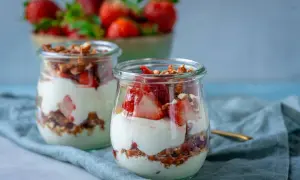 Erdbeer-Dessert im Glas mit Joghurt und Granola, im Hintergrund eine Schüssel mit Erdbeeren.