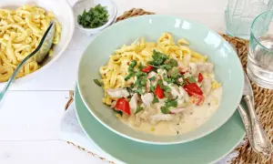 Nudeln mit Hähnchen in cremiger Soße, garniert mit Petersilie und Paprika.