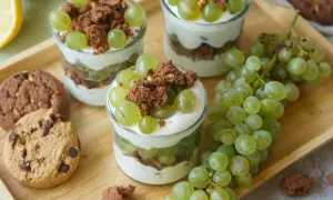 Drei Gläser mit Trauben-Keks-Dessert, garniert mit grünen Trauben und Schokostückchen, daneben Kekse und Trauben.