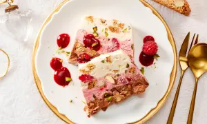 Gefrorenes Dessert mit Schichten aus Schokolade, Beeren und Nüssen, garniert mit Beeren und Sauce.