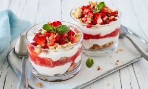 Zwei Gläser mit geschichtetem Erdbeer-Mascarpone-Dessert, garniert mit Minze und Keksbröseln.