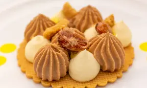 Ein kunstvolles Dessert mit braunen und hellen Cremetupfern, Nüssen und gelben Tupfern auf einem Keks.