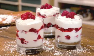 Drei Gläser mit Himbeer-Mascarpone-Dessert, garniert mit frischen Himbeeren und Kokosraspeln.