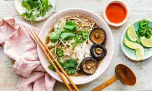 Vegetarische Pho mit Pilzen, Limette, Koriander und Jalapeños, serviert mit Sojasauce und Stäbchen.