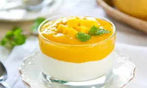 Cremiges Mango-Joghurt-Dessert im Glas, garniert mit Mangostücken und Minze.