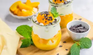 Zwei Gläser mit Schichtdessert aus Pfirsich und Sahne, garniert mit Schokostreuseln und Minze.