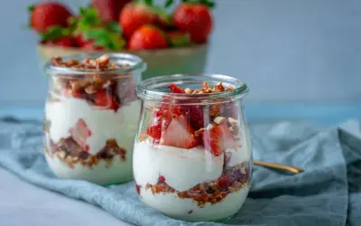 Erdbeer-Dessert im Glas mit Joghurt und Granola, im Hintergrund eine Schüssel mit Erdbeeren.