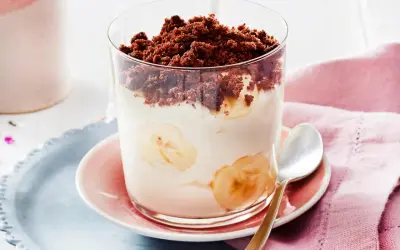 Dessert im Glas mit Bananenscheiben, Sahne und Schokostreuseln.