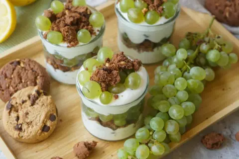 Drei Gläser mit Trauben-Keks-Dessert, garniert mit grünen Trauben und Schokostückchen, daneben Kekse und Trauben.
