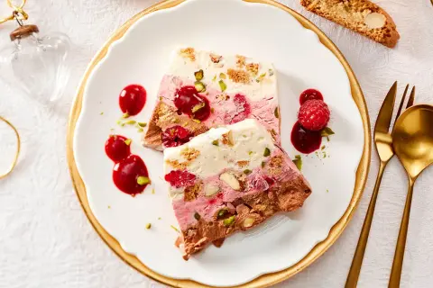 Gefrorenes Dessert mit Schichten aus Schokolade, Beeren und Nüssen, garniert mit Beeren und Sauce.