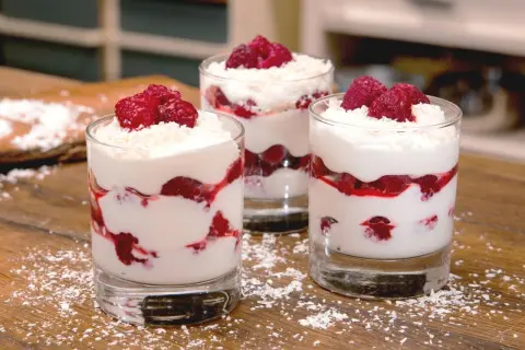 Drei Gläser mit Himbeer-Mascarpone-Dessert, garniert mit frischen Himbeeren und Kokosraspeln.
