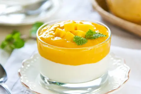 Cremiges Mango-Joghurt-Dessert im Glas, garniert mit Mangostücken und Minze.