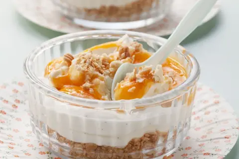Schichtdessert mit Mascarpone, Fruchtpüree und Keksbröseln in einem Glas.