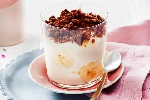 Dessert im Glas mit Bananenscheiben, Sahne und Schokostreuseln.