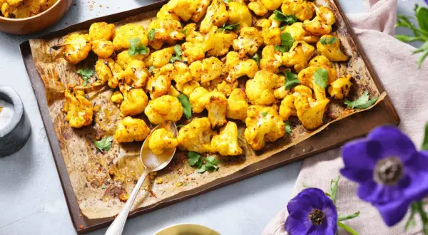 Gerösteter Blumenkohl mit Kräutern auf einem Backblech, daneben eine Schüssel mit Dip.