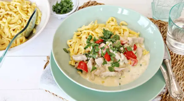 Nudeln mit Hähnchen in cremiger Soße, garniert mit Petersilie und Paprika.
