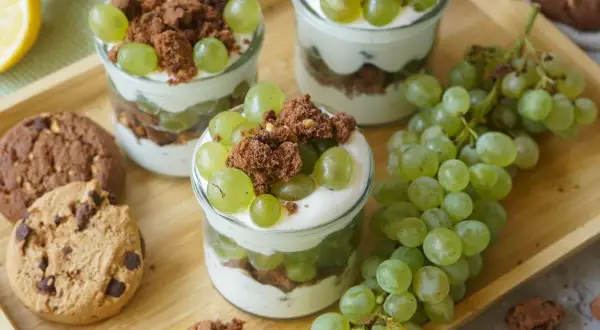 Drei Gläser mit Trauben-Keks-Dessert, garniert mit grünen Trauben und Schokostückchen, daneben Kekse und Trauben.