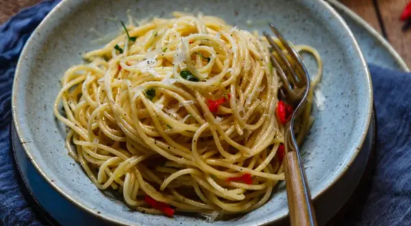 Spaghetti Aglio e Olio mit Chili und Parmesan in einer Schüssel, daneben eine Gabel.
