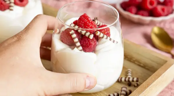 Cremiges Mascarpone-Dessert mit Himbeeren und Schokoröllchen im Glas.