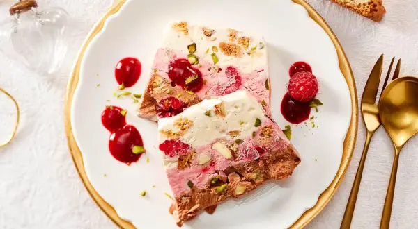 Gefrorenes Dessert mit Schichten aus Schokolade, Beeren und Nüssen, garniert mit Beeren und Sauce.
