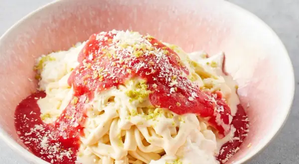 Spaghettieis mit Erdbeersoße und Kokosraspeln in einer rosa Schale.