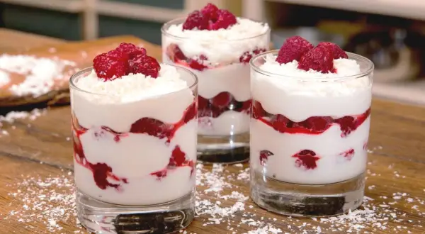 Drei Gläser mit Himbeer-Mascarpone-Dessert, garniert mit frischen Himbeeren und Kokosraspeln.