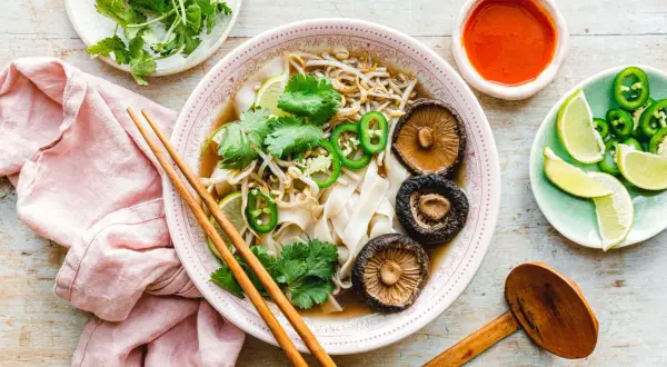 Vegetarische Pho mit Pilzen, Limette, Koriander und Jalapeños, serviert mit Sojasauce und Stäbchen.