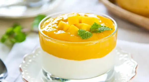 Cremiges Mango-Joghurt-Dessert im Glas, garniert mit Mangostücken und Minze.