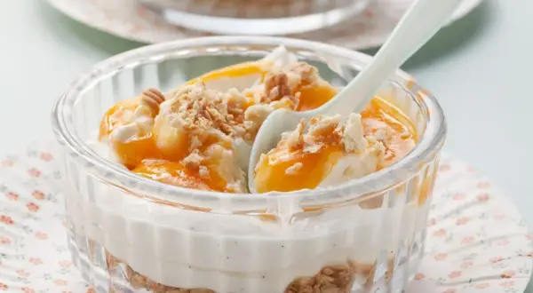 Schichtdessert mit Mascarpone, Fruchtpüree und Keksbröseln in einem Glas.