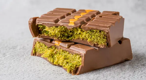 Gestapelte Schokoladenriegel mit grüner Pistazienfüllung und orangen Akzenten.
