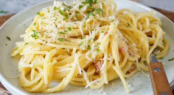 Spaghetti Carbonara mit geriebenem Parmesan und Petersilie auf einem Teller.