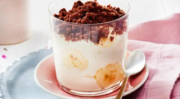Dessert im Glas mit Bananenscheiben, Sahne und Schokostreuseln.
