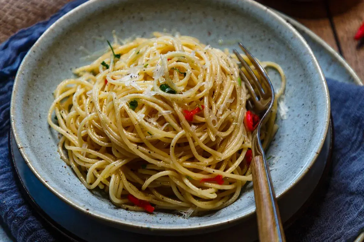 Spaghetti Aglio e Olio mit Chili und Parmesan in einer Schüssel, daneben eine Gabel.