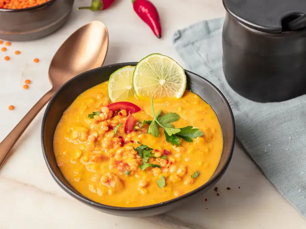 cremige Linsen-Curry-Suppe in einer Schale mit frischem Koriander und einem L&ouml;ffel
