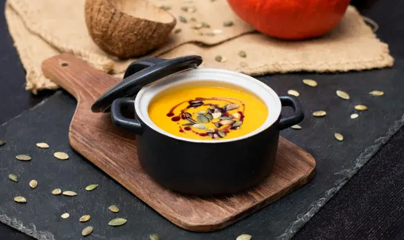 Cremige K&uuml;rbis-Curry-Suppe in einer Schale mit Toppings wie K&uuml;rbiskernen und Koriander