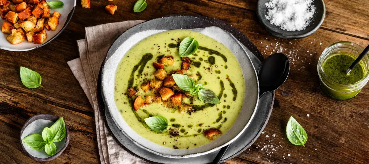 cremige Zucchinisuppe in einer Schüssel mit frischen Kräutern und einem Löffel