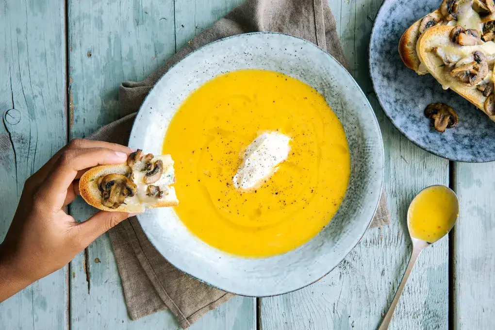 cremige K&uuml;rbissuppe in einer Schale mit K&uuml;rbiskernen und einem L&ouml;ffel serviert