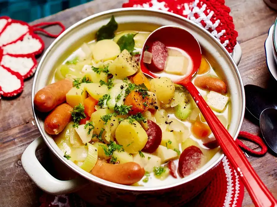 Gro&szlig;er Topf mit dampfender Kartoffelsuppe auf einem rustikalen Holztisch mit L&ouml;ffeln und Sch&uuml;sseln