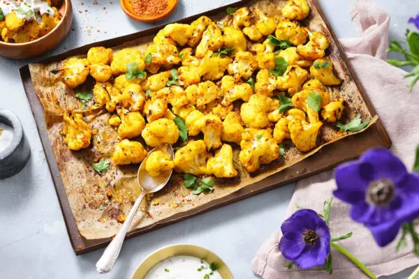 Gerösteter Blumenkohl mit Kräutern auf einem Backblech, daneben eine Schüssel mit Dip.