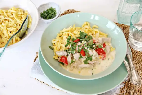 Nudeln mit Hähnchen in cremiger Soße, garniert mit Petersilie und Paprika.