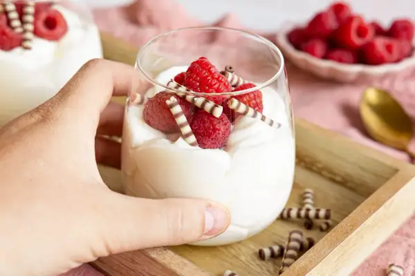 Cremiges Mascarpone-Dessert mit Himbeeren und Schokoröllchen im Glas.