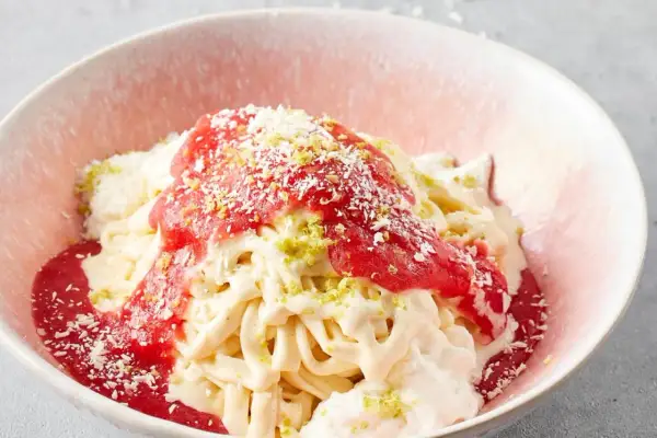 Spaghettieis mit Erdbeersoße und Kokosraspeln in einer rosa Schale.