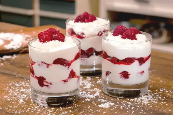 Drei Gläser mit Himbeer-Mascarpone-Dessert, garniert mit frischen Himbeeren und Kokosraspeln.
