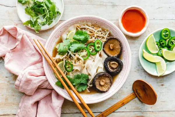 Vegetarische Pho mit Pilzen, Limette, Koriander und Jalapeños, serviert mit Sojasauce und Stäbchen.