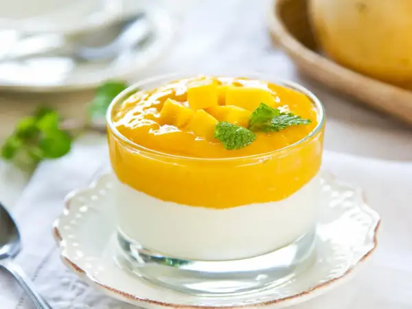 Cremiges Mango-Joghurt-Dessert im Glas, garniert mit Mangostücken und Minze.