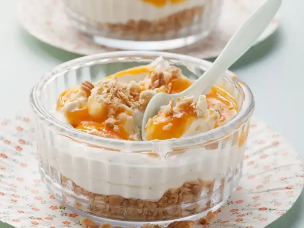 Schichtdessert mit Mascarpone, Fruchtpüree und Keksbröseln in einem Glas.