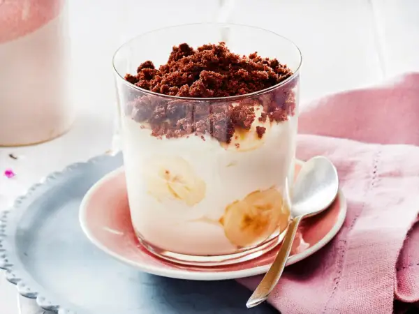 Dessert im Glas mit Bananenscheiben, Sahne und Schokostreuseln.